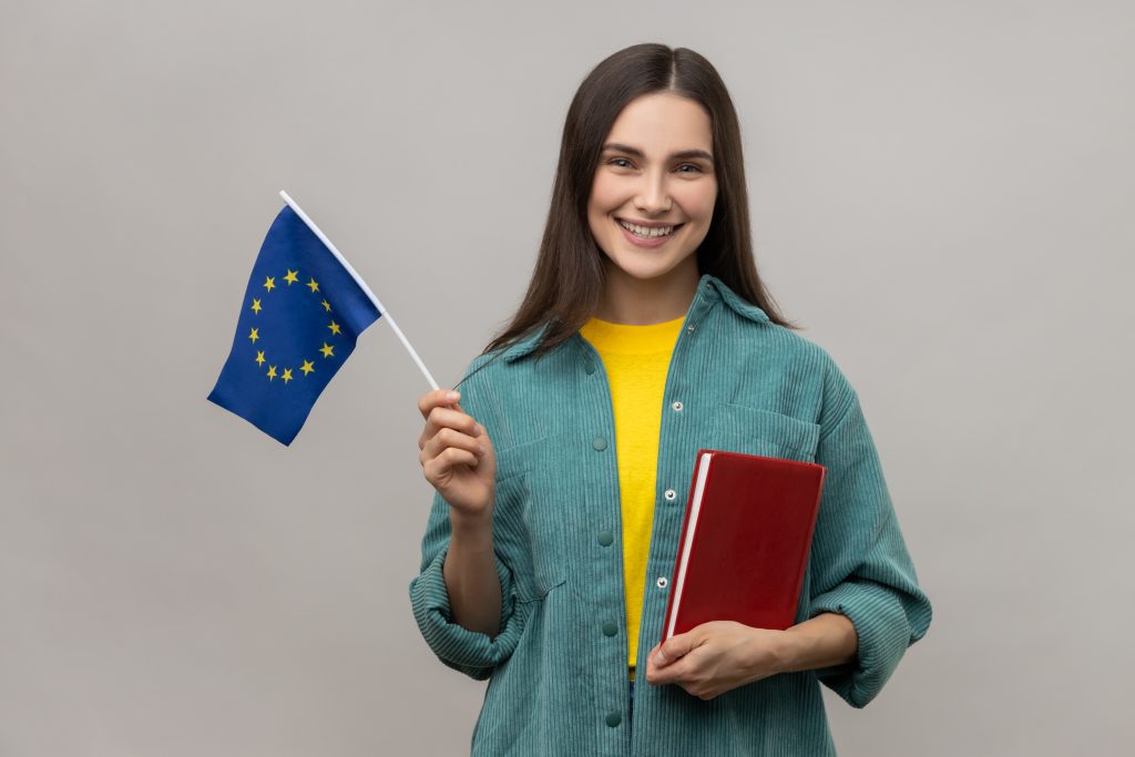 portrait positive student woman holding books europe union flag education abroad looking smiling camera wearing casual style jacket indoor studio shot isolated gray background scaled